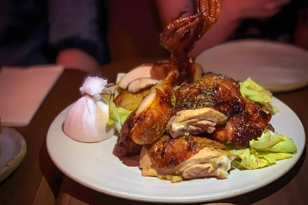 Roasted chicken pieces on a white plate garnished with lettuce. Beside it is a small wrapped package. Atmosphere is cozy and inviting.