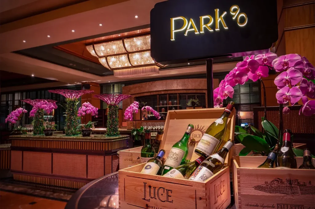 Luxurious dining setting at Park90 with ornate chandeliers, vibrant pink orchids, and wooden crates of wine bottles, exuding elegance and sophistication.