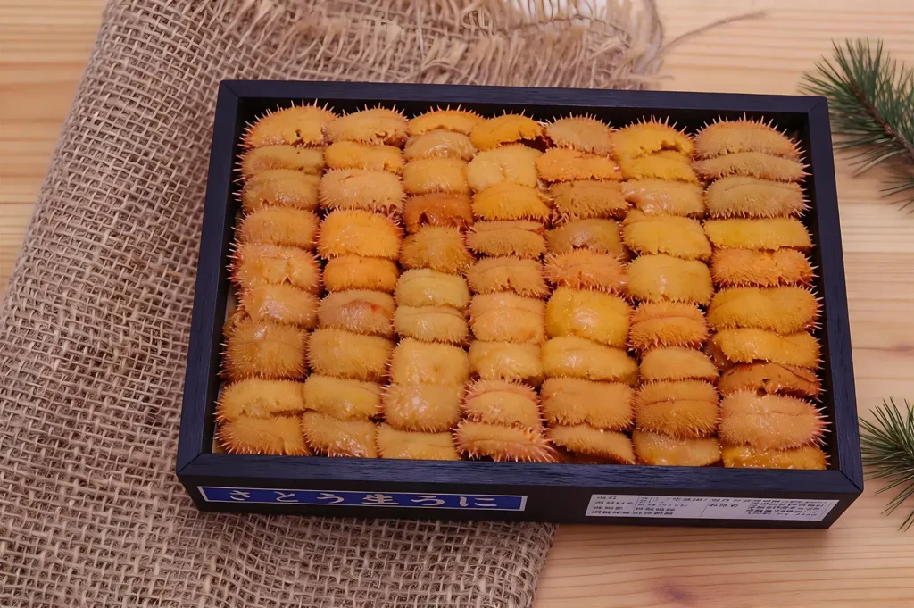 A black tray filled with neatly arranged, bright orange sea urchin roe, set on a textured burlap mat. The scene suggests freshness and delicacy.