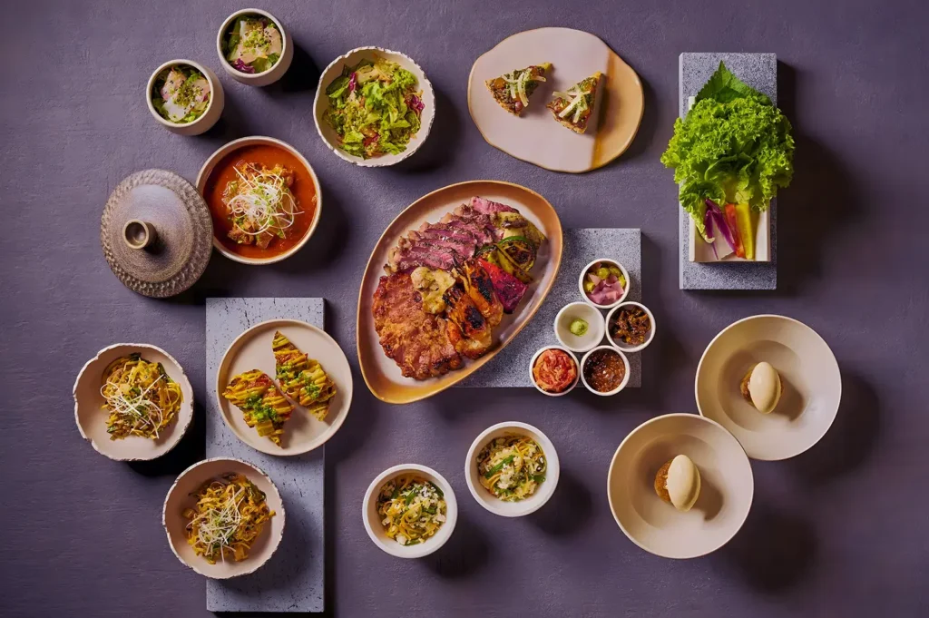 A variety of elegantly plated Asian dishes on a dark surface, including dumplings, meats, salads, and sides, creating a harmonious and appetizing display.