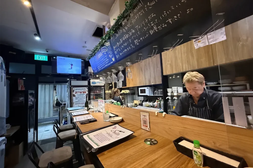 Al Solito Japanese bar counter interior at Cuppage Plaza with chef preparing food behind a wooden bar.