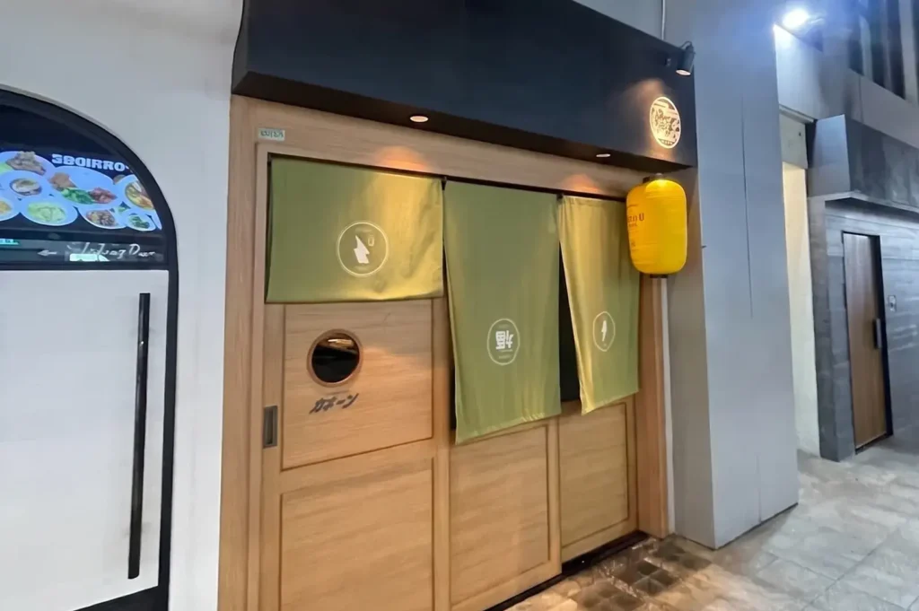 Kakiin Oyster Bar Japanese restaurant storefront at Cuppage Plaza with green noren curtains and wooden sliding doors.