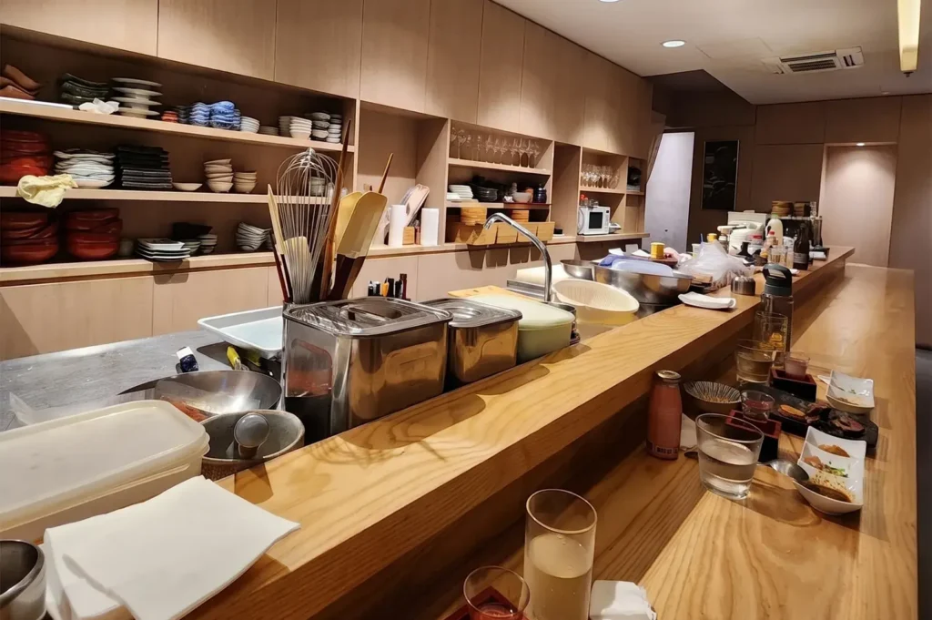 Bistro Du Le Pin Japanese restaurant open kitchen counter dining area at Cuppage Plaza with light wood finishes and tableware shelves.