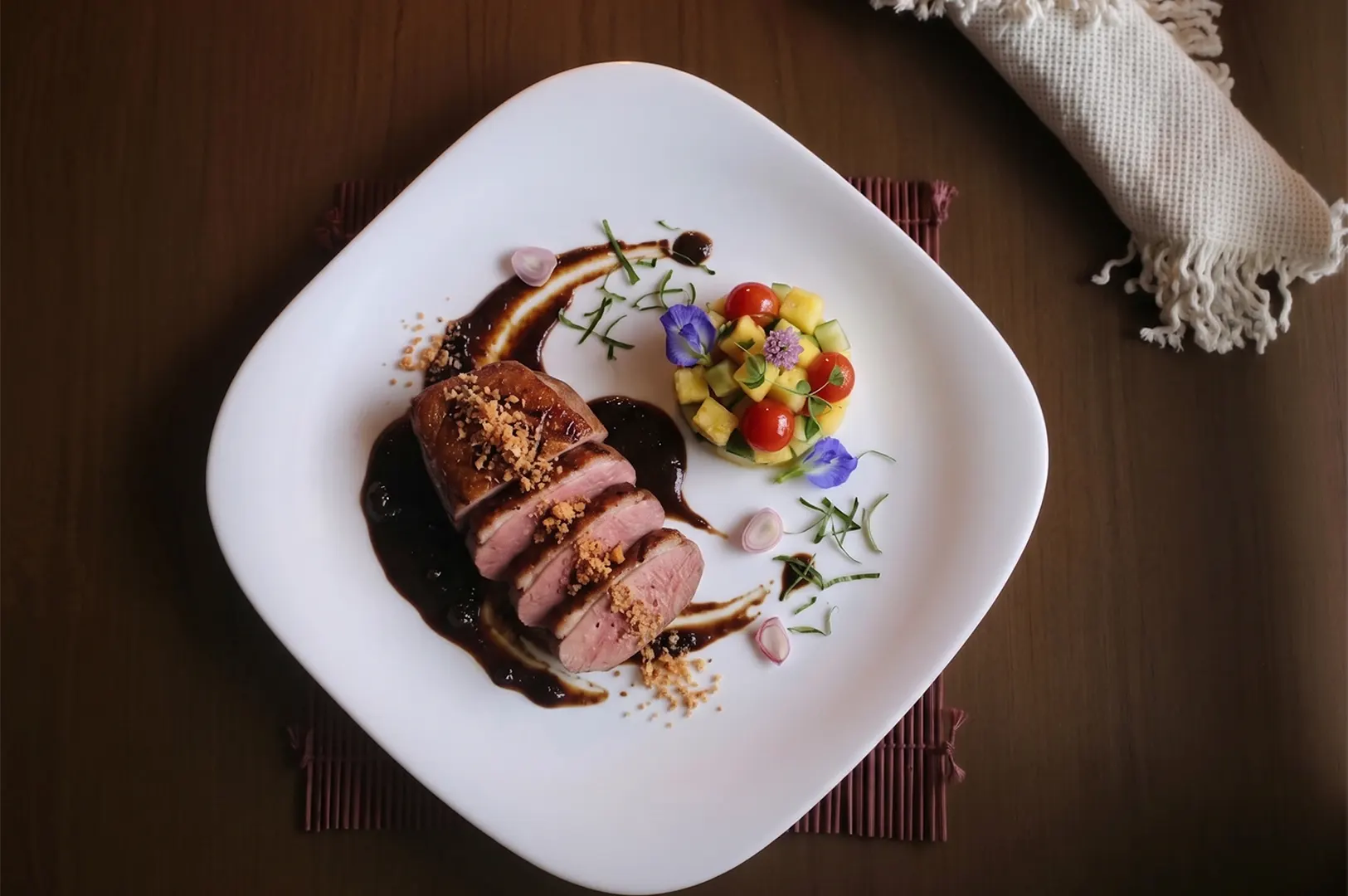 Sliced roasted duck breast with dark sauce and mango tomato salsa on a white plate.