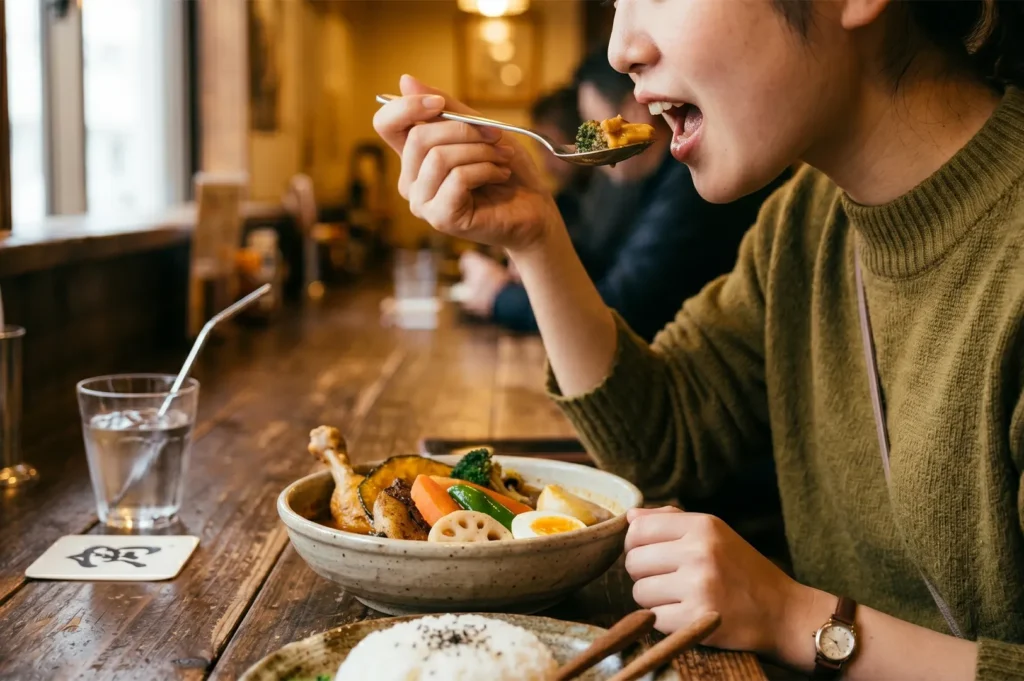 A woman eating Japanese soup curry with a spoon at a wooden restaurant counter.