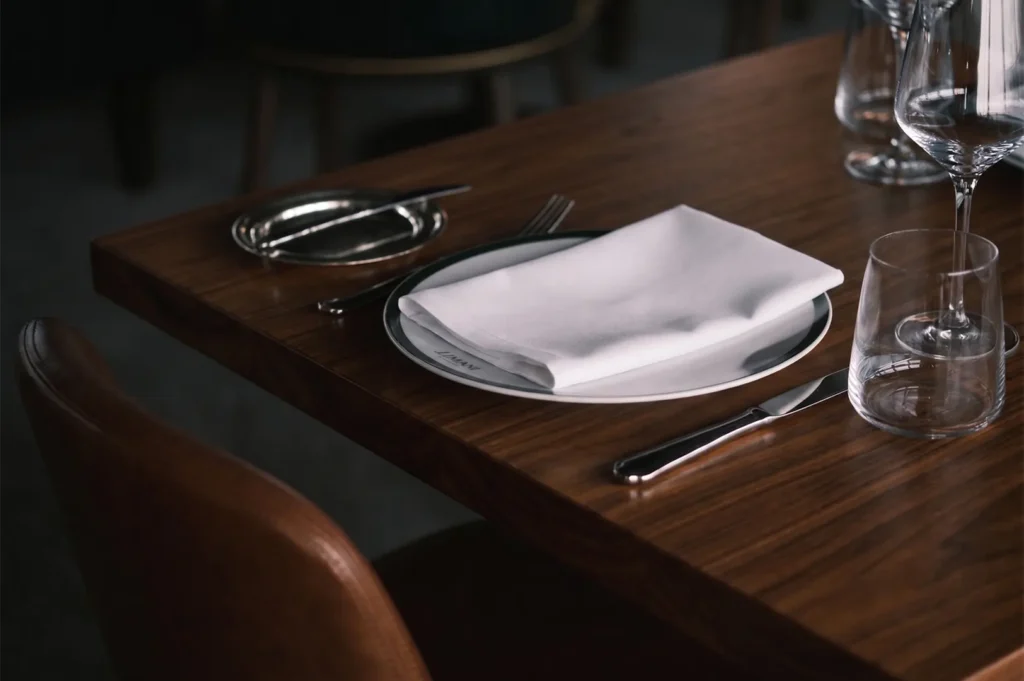 Fine dining table setting with a white napkin on a plate, wine glass, and wooden table.