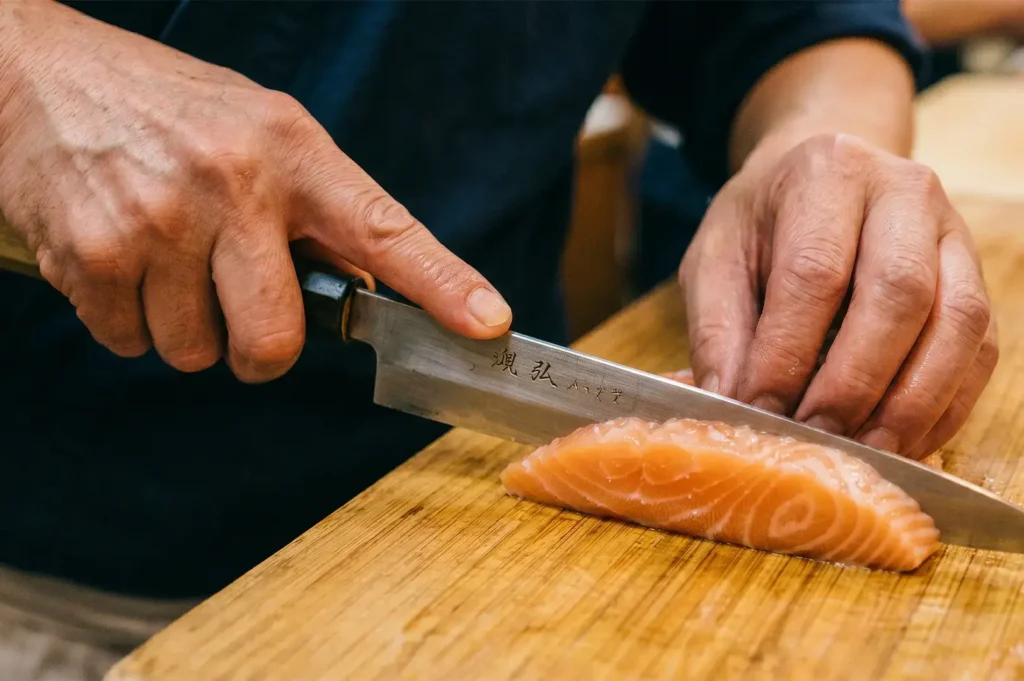 Japanese sushi chef slicing fresh salmon sashimi with a traditional Yanagiba knife.