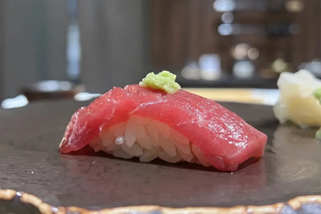 Fresh tuna nigiri sushi topped with wasabi on a ceramic plate.