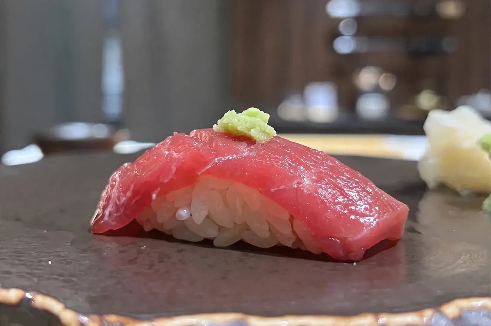 Fresh tuna nigiri sushi topped with wasabi on a ceramic plate.
