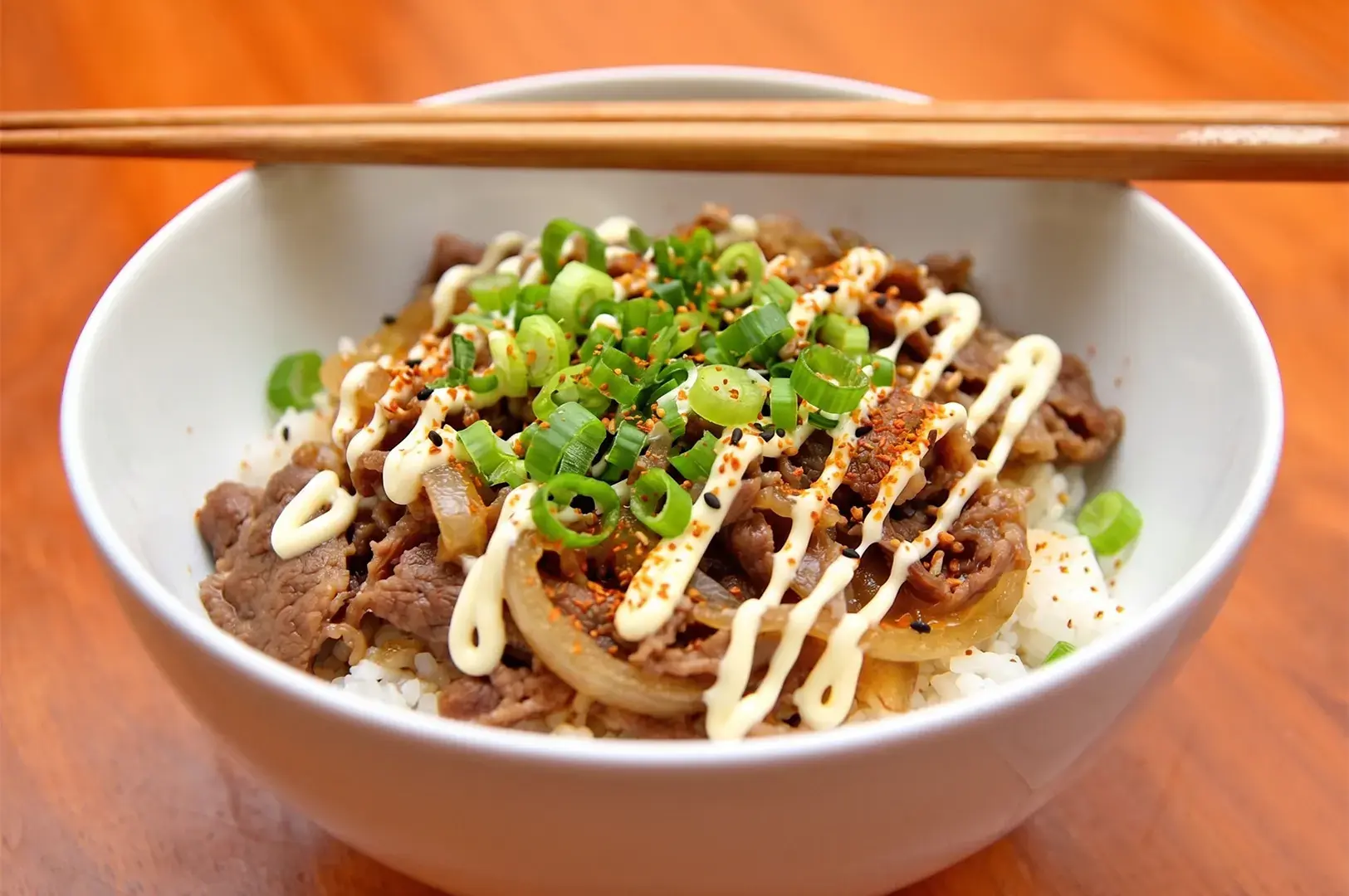 Japanese beef bowl Gyudon with mayo, green onions, and chopsticks.