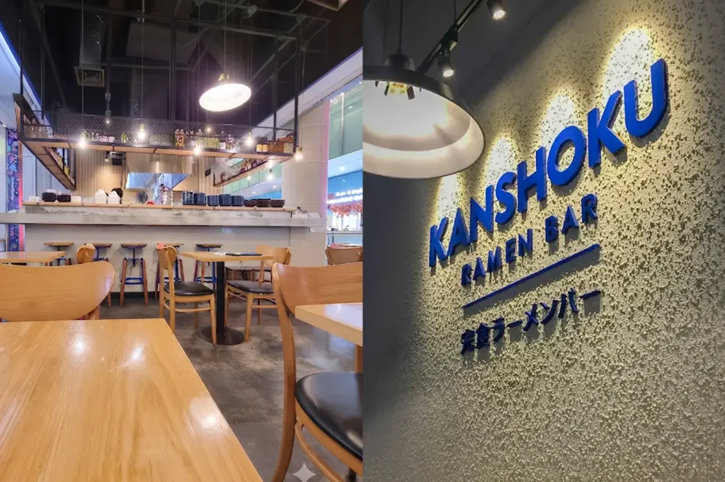 Interior view of Kanshoku Ramen Bar featuring wooden tables, seating, and the restaurant's signage on a textured wall.