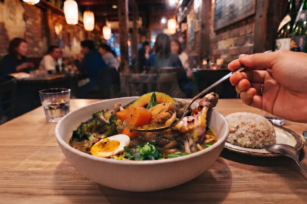 Person eating Japanese soup curry with chicken, vegetables, and rice at a dimly lit restaurant.