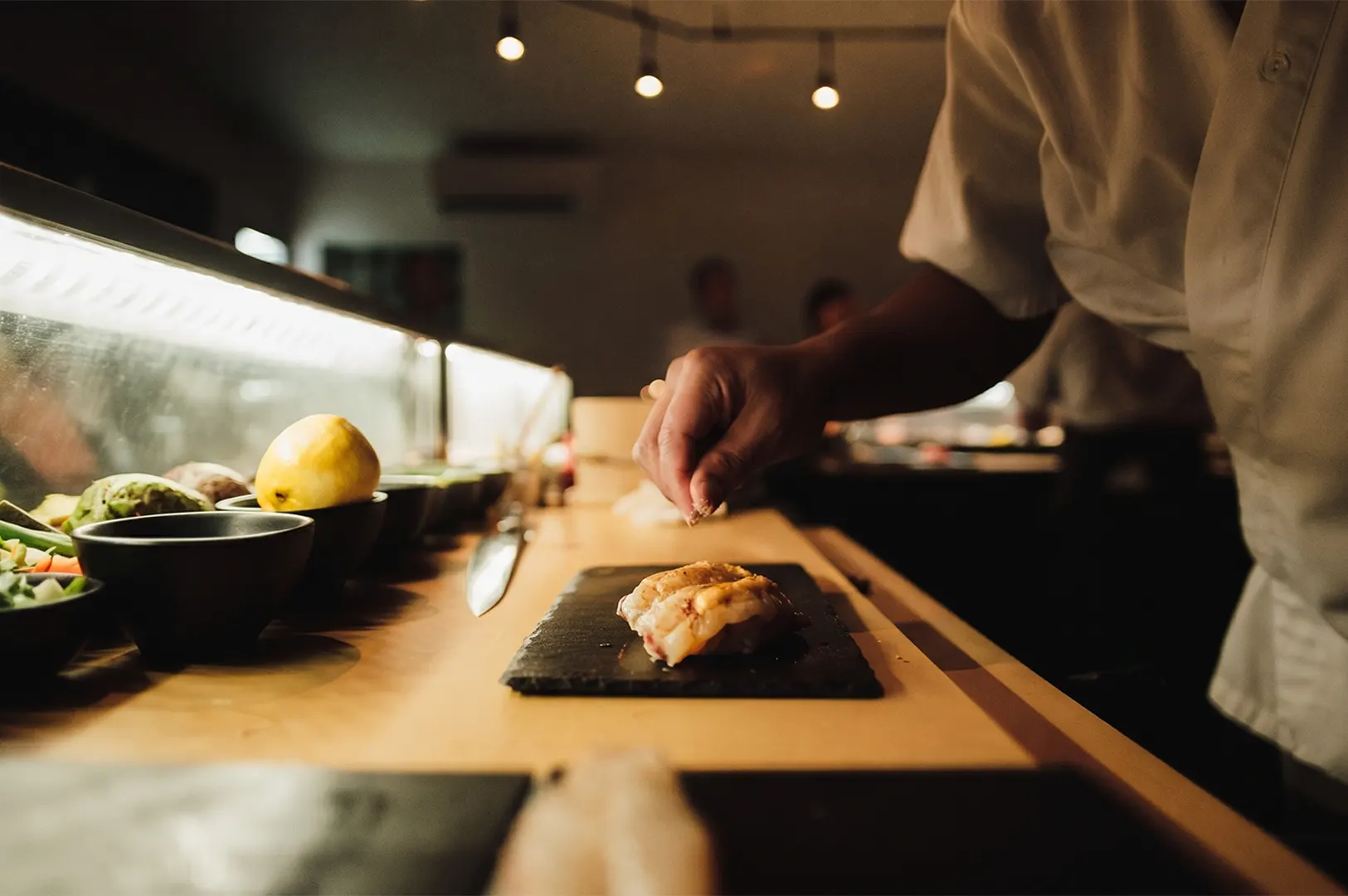 Chef preparing fresh sushi on a stone plate in a restaurant kitchen.